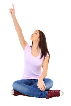 Attractive teenage girl sitting on the floor and pointing with finger. All on white background.