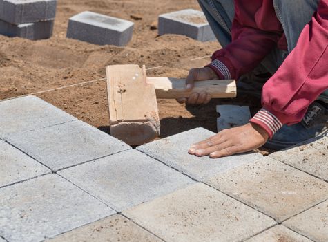 The worker is paving a stone path with wooden hammer