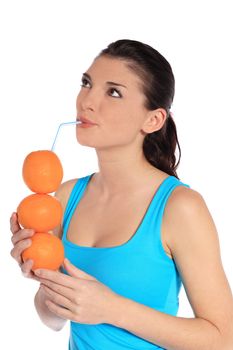 Attractive young woman drinking orange juice out of stacked oranges. All on white background.