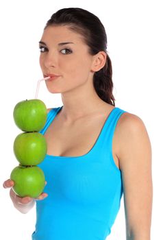 Attractive young woman drinking apple juice out of stacked green apples. All on white background.