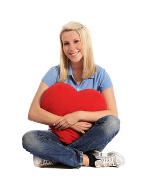 An attractive young woman sitting on the floor, hugging a heart-shaped pillow. All on white background.