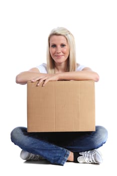 Attractive young woman sitting on floor holding moving box. All on white background.