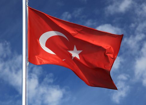 Turkish flag in front of light cloudy sky.