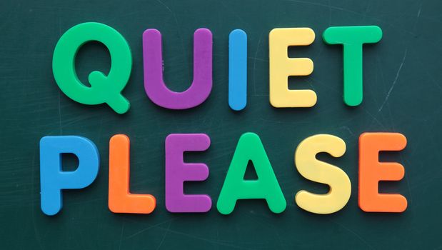 The term quiet please in colorful letters on a blackboard.