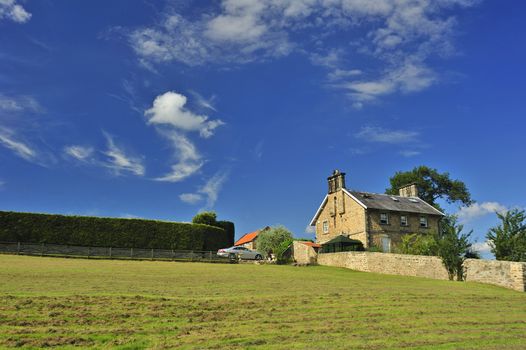 A stone farmhouse on a hillside, under a summer sky.