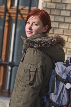 Image of a redheaded girl student with a backpack in front of the University building.