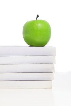 A green apple lies on a pile of books, symbolizing studies. All on white background.