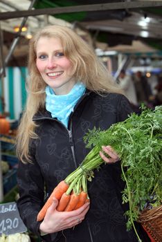 Woman buys vegetables in the market.She carries carrots in hand