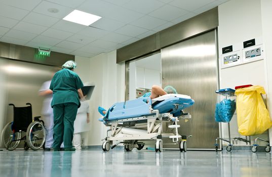 People with medical uniforms and patient lying on trolley in hospital corridor