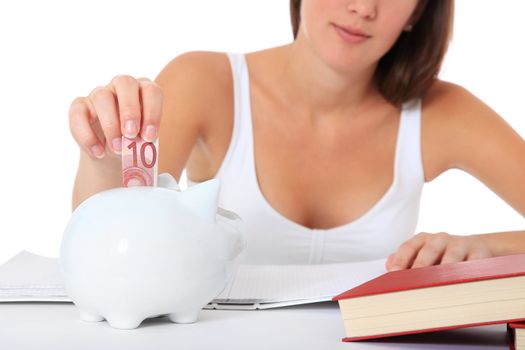 Attractive young student puts money in her piggy bank. All on white background.