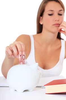 Attractive young student puts money in her piggy bank. All on white background.