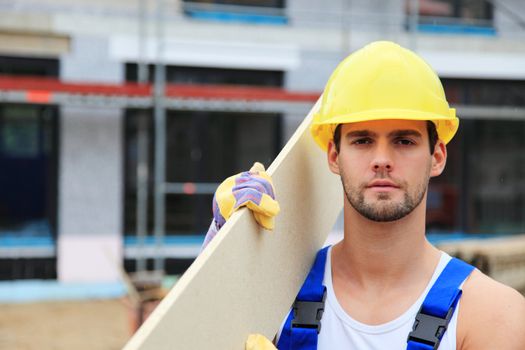 Manual worker on construction site carrying wooden board.