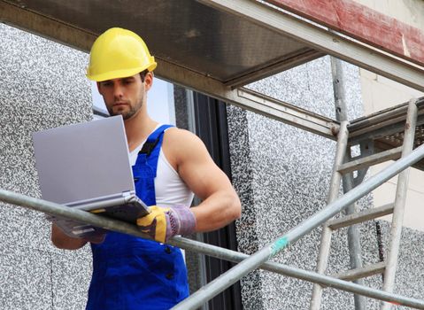 Manual worker on construction site using laptop.