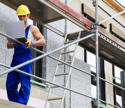 Manual worker on construction site using laptop.