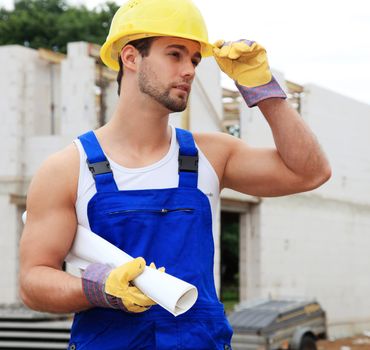 Manual worker on construction site holding plans.