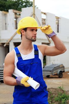 Manual worker on construction site holding plans.