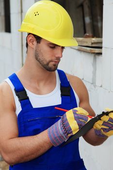 Manual worker on construction site writing on clipboard.