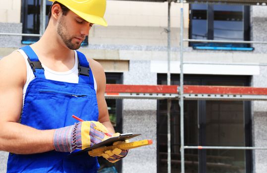 Manual worker on construction site writing on clipboard.