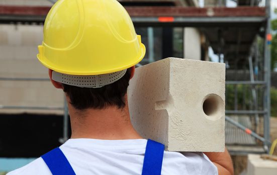 Manual worker on construction site carrying brick.