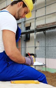 Manual worker on construction site writing on clipboard.