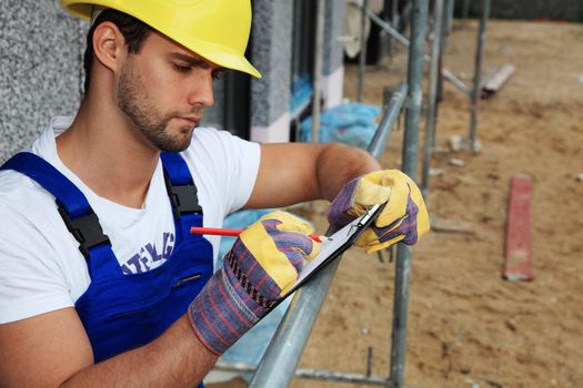 Manual worker on construction site writing on clipboard.