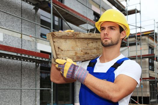 Manual worker on construction site carrying wooden board.