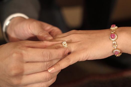 groom putting a wedding diamond ring on bride 's finger