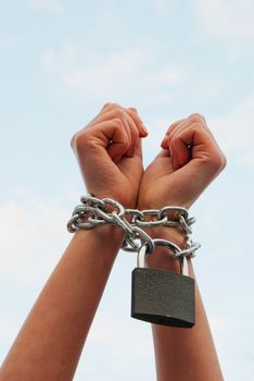 Woman's hands tied up with chains against blue sky