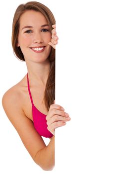 Attractive young woman in bikini standing behind white wall looking at blank sign. All on white background.