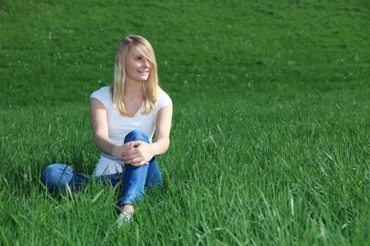 Attractive young woman resting outside on green meadow.