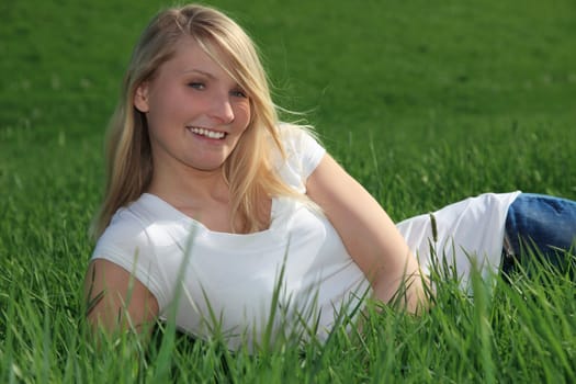 Attractive young woman resting outside on green meadow.