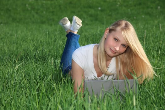 Attractive young woman resting outside on green meadow using a notebook.