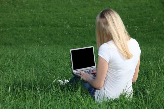 Attractive young woman resting outside on green meadow using a notebook image.