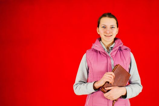 Teen girl staying with a book against red background