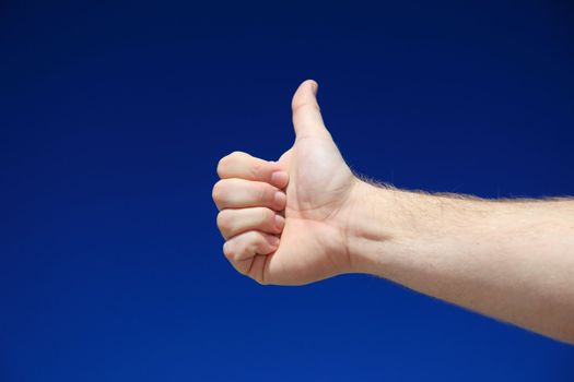 A persons hand making thumbs up sign in front of bright blue sky.