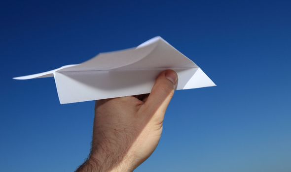 A persons hand holding a paper plane in front of bright blue sky.