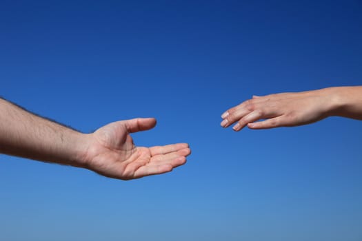 Two persons trying to reach hands. All in front of bright blue sky.