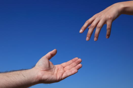 Two persons trying to reach hands. All in front of bright blue sky.