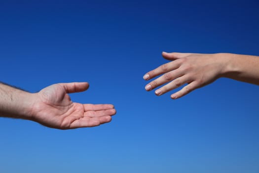 Two persons trying to reach hands. All in front of bright blue sky.