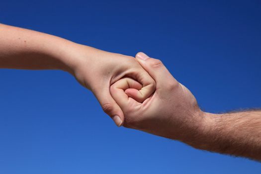 Two persons holding hands in front of bright blue sky.