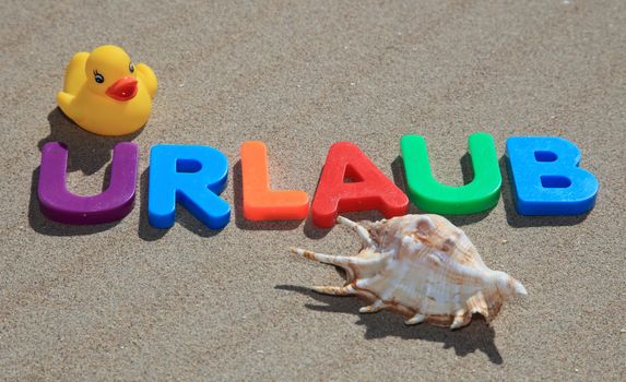 The German term urlaub (Engl.: holiday) written in colorful letters on the sand.