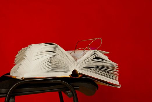 Open book laying on the chair against red background