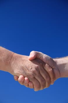 Two persons shaking hands in front of bright blue sky.