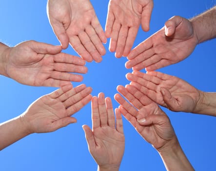 Various peoples hands in front of bright blue sky.