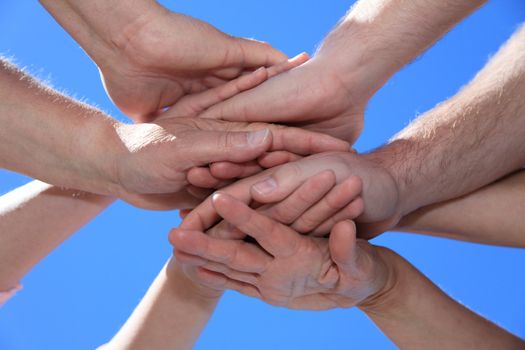 Various peoples hands in front of bright blue sky.