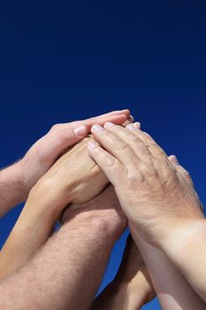 Various peoples hands in front of bright blue sky.