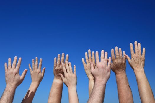 Various peoples hands in front of bright blue sky.