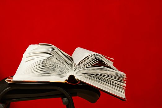 Open book laying on the chair against red background