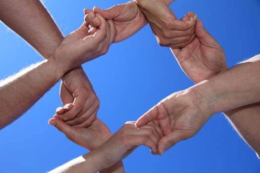 Various peoples hands in front of bright blue sky.