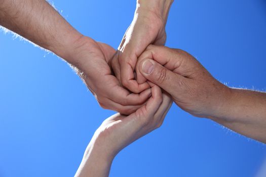 Various peoples hands in front of bright blue sky.